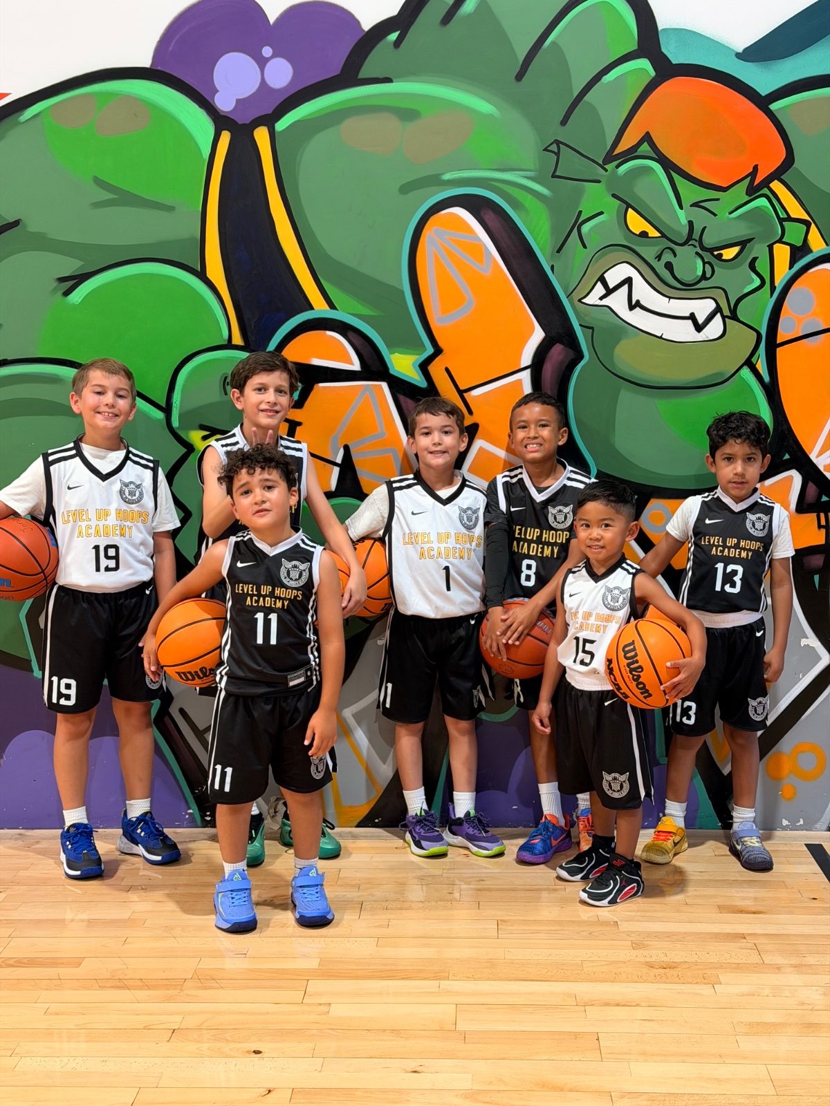 Level Up Hoops youth squad with basketballs in front of mural